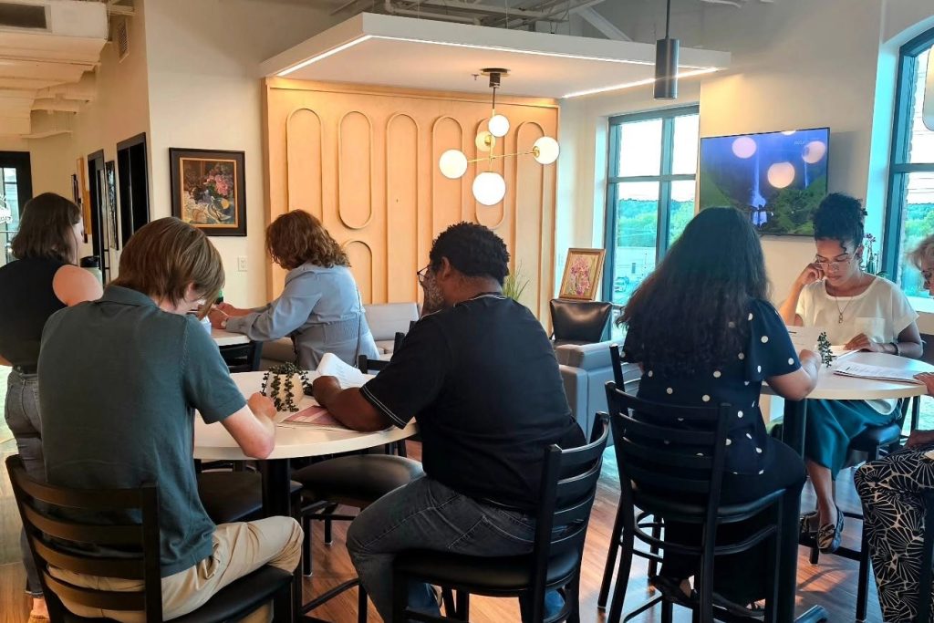 A room of community actors reading from scripts at round tables during a read-through